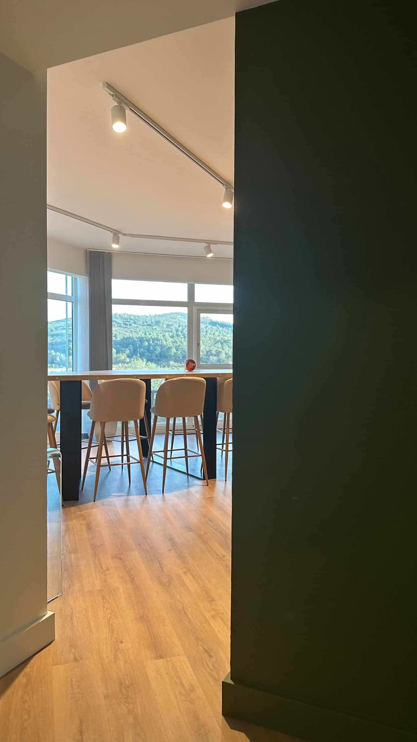 Table haute, tabourets beiges et vue sur collines verdoyantes dans un intérieur moderne lumineux.
