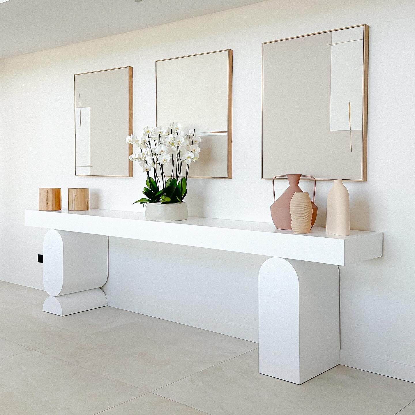 Console blanche, orchidée et vases sous trois cadres abstraits. Décoration zen et épurée.