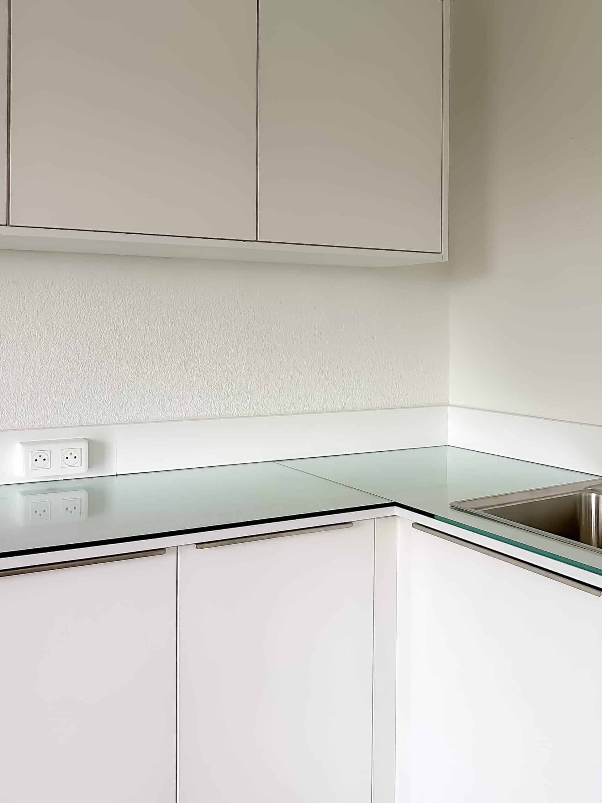 Cuisine moderne blanche avec plan de travail en verre, placards épurés et évier en inox.