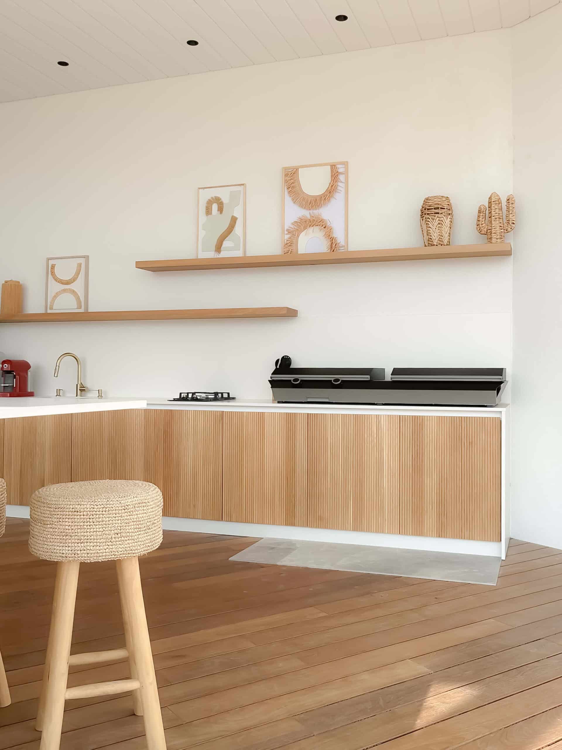 Cuisine minimaliste : meubles en bois clair, étagères et tabouret tressé dans un décor épuré lumineux.