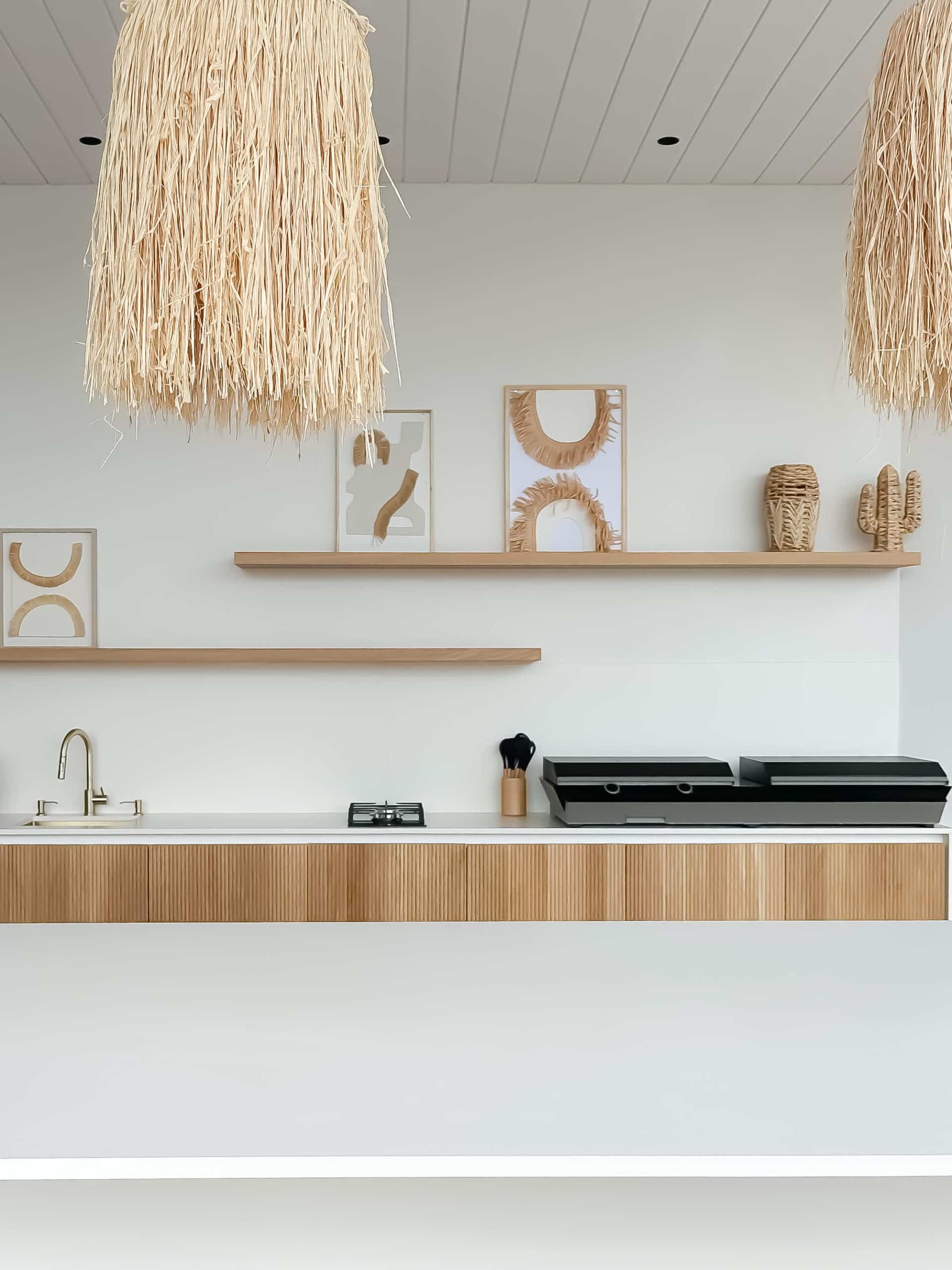 Cuisine bohème : suspensions en paille, étagères en bois et meubles cannelés sur mur blanc minimaliste.