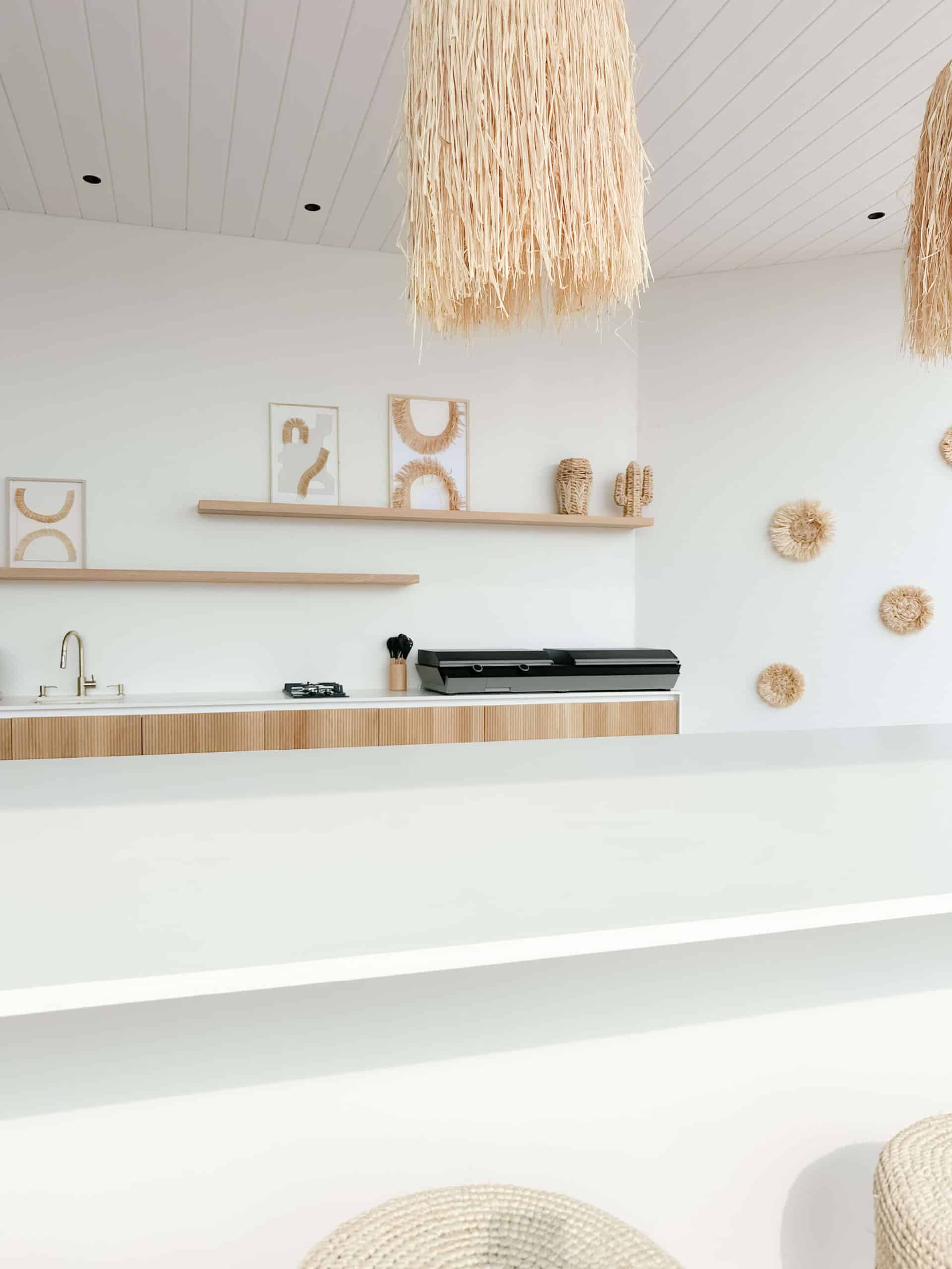 Cuisine minimaliste bohème blanche avec étagères en bois et suspensions en fibres naturelles.