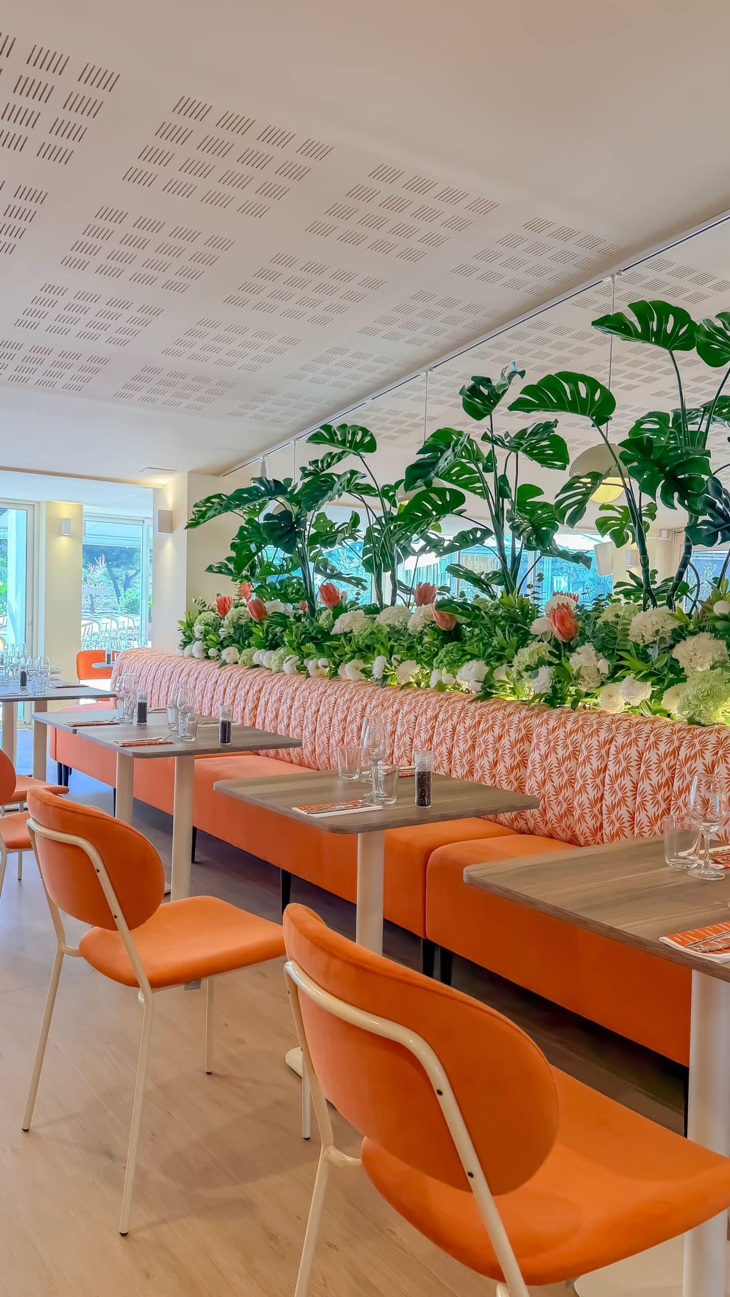 Salle de restaurant moderne, chaises orange et décor tropical luxuriant.
