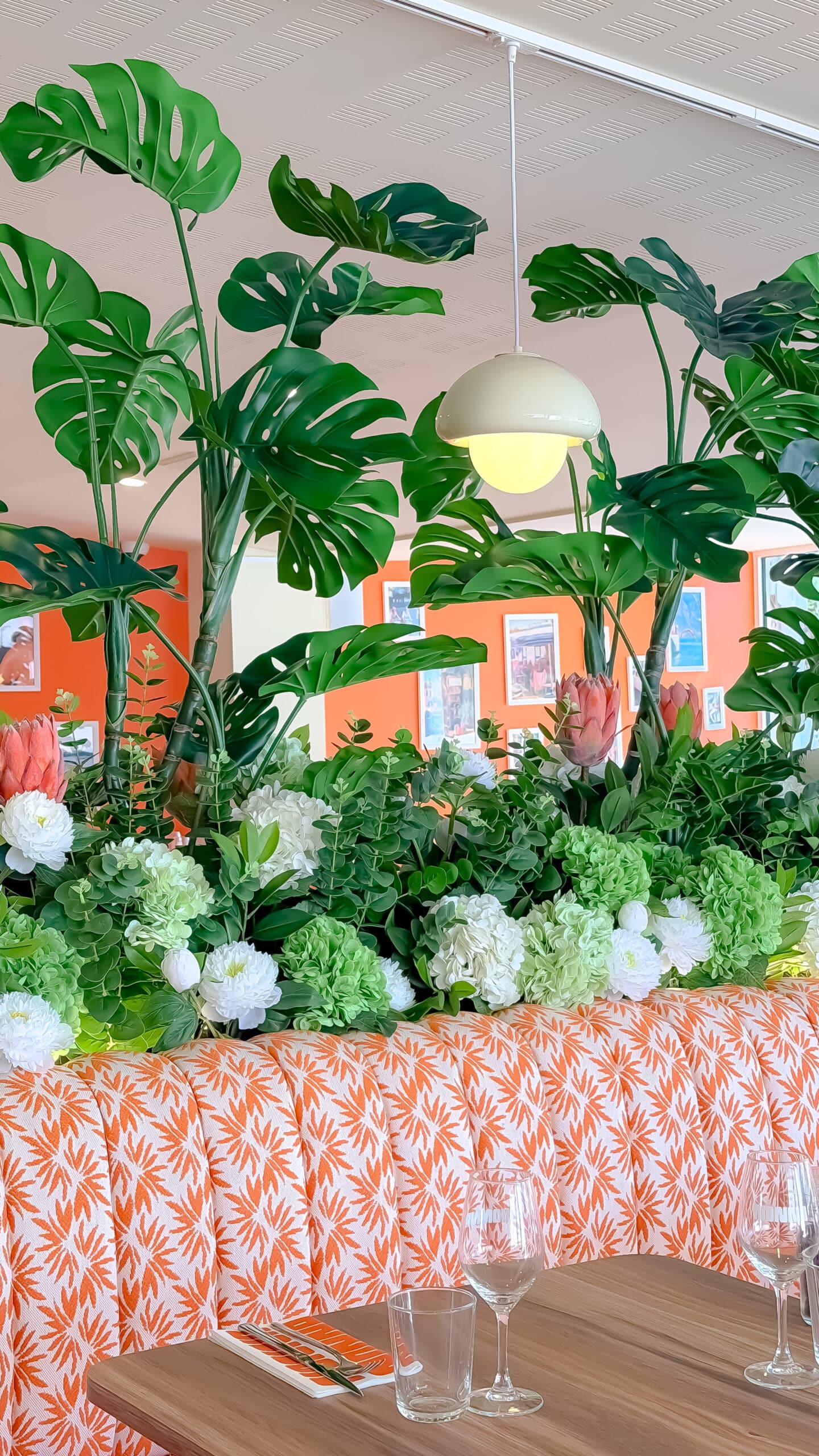 Banquette orange à motifs sous des feuilles de Monstera et hortensias dans un restaurant moderne.