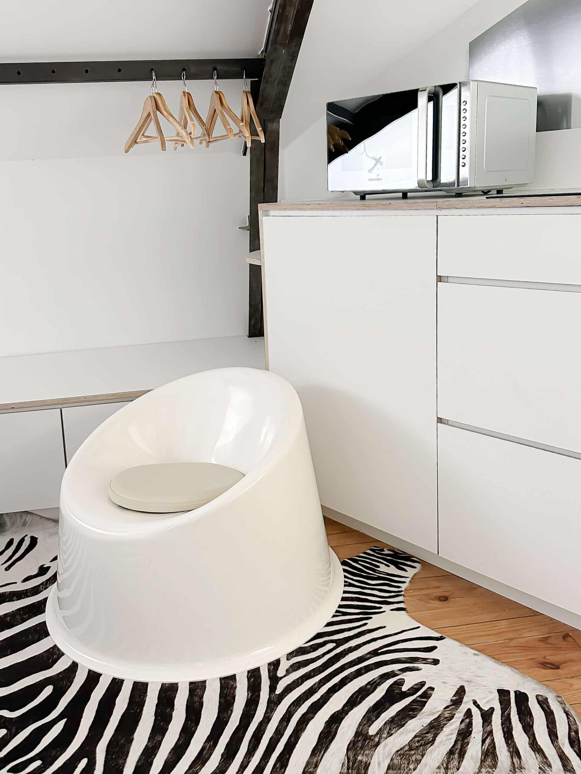 Fauteuil blanc design, tapis zèbre, meuble blanc avec micro-ondes Medion et cintres en bois.