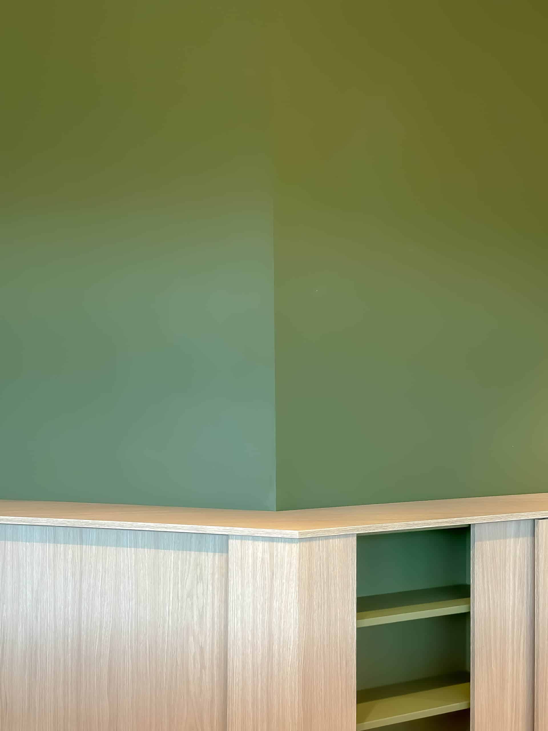 Angle de mur vert olive et rangement en bois clair au design épuré.