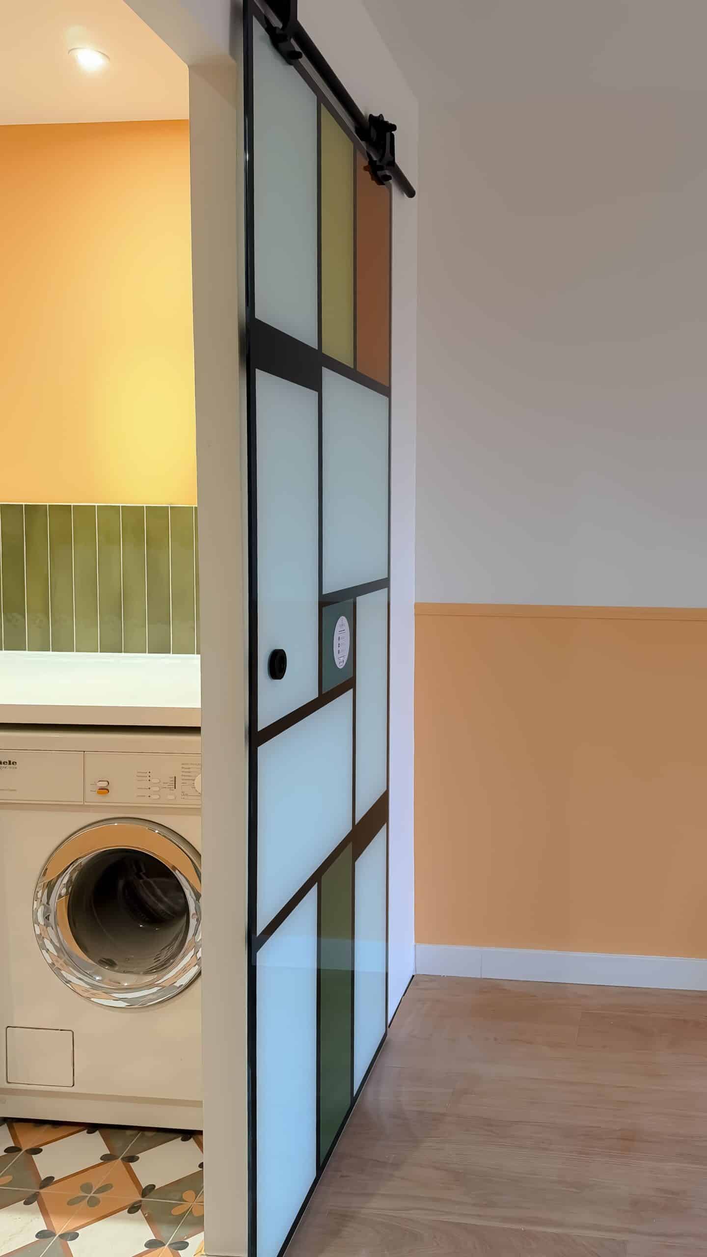 Porte coulissante géométrique style Mondrian devant une buanderie avec lave-linge Miele.