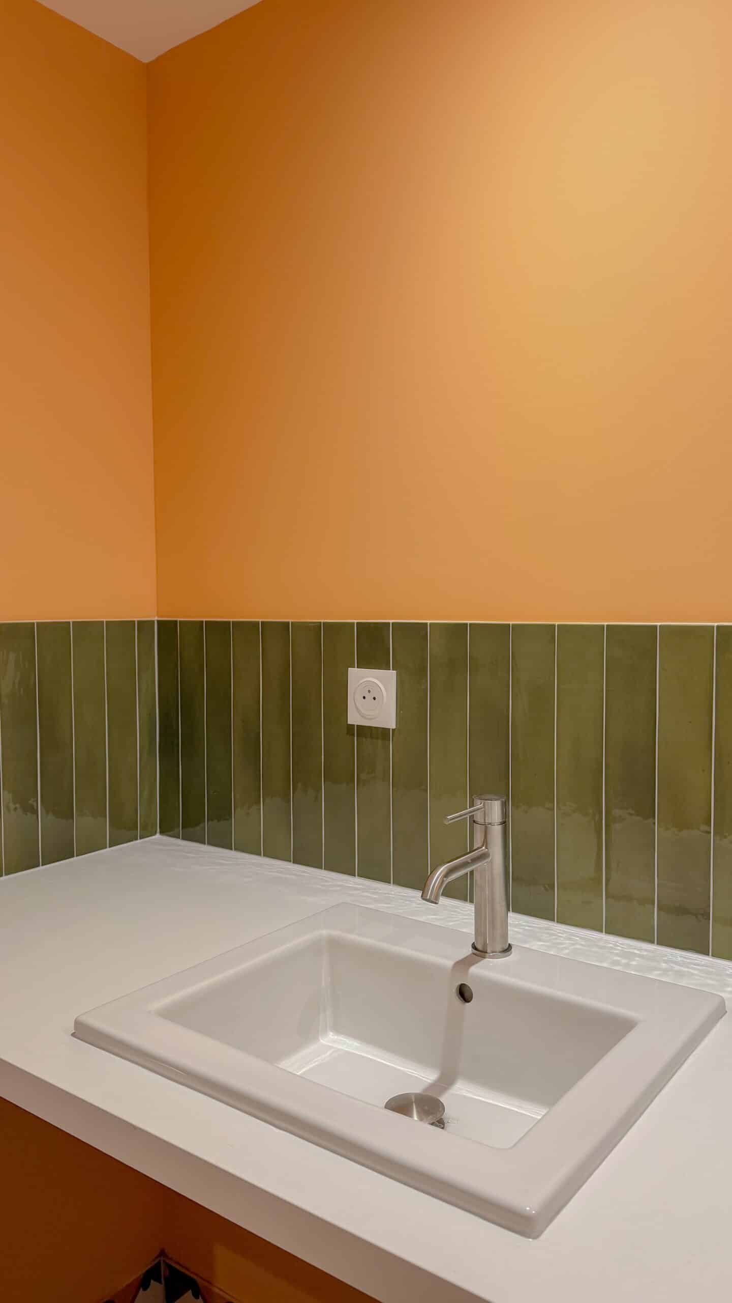 Vasque blanche, dosseret carrelage vert vertical, mur orange vif et robinet chromé moderne.