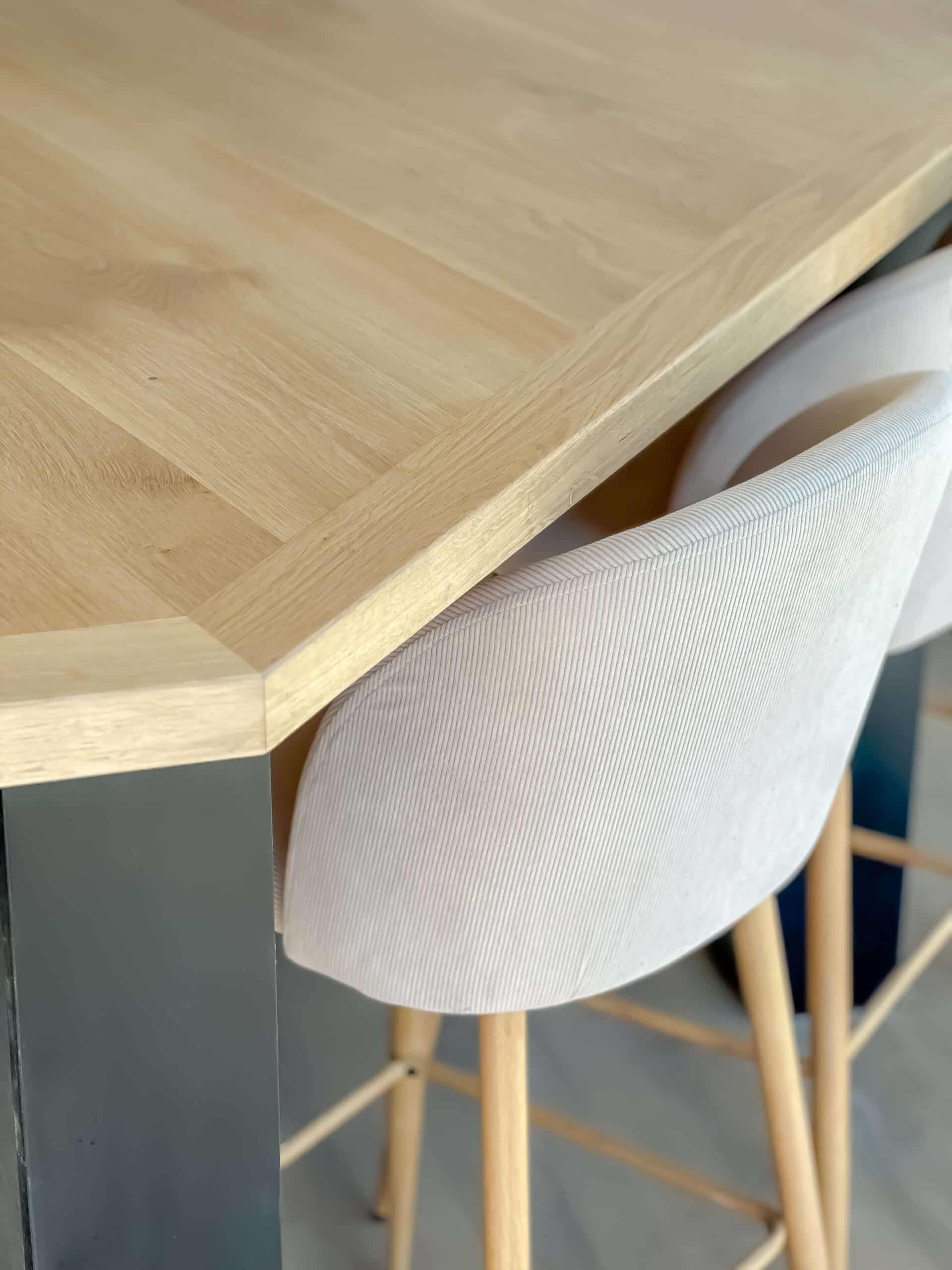 Détail d'une table en chêne clair et d'un tabouret haut en velours côtelé blanc.
