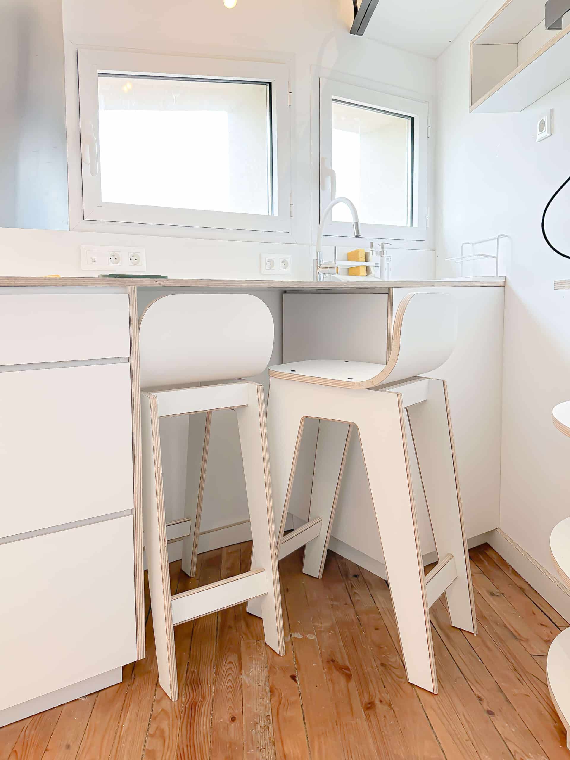 Cuisine blanche minimaliste, tabourets design en bois clair, évier et parquet naturel.