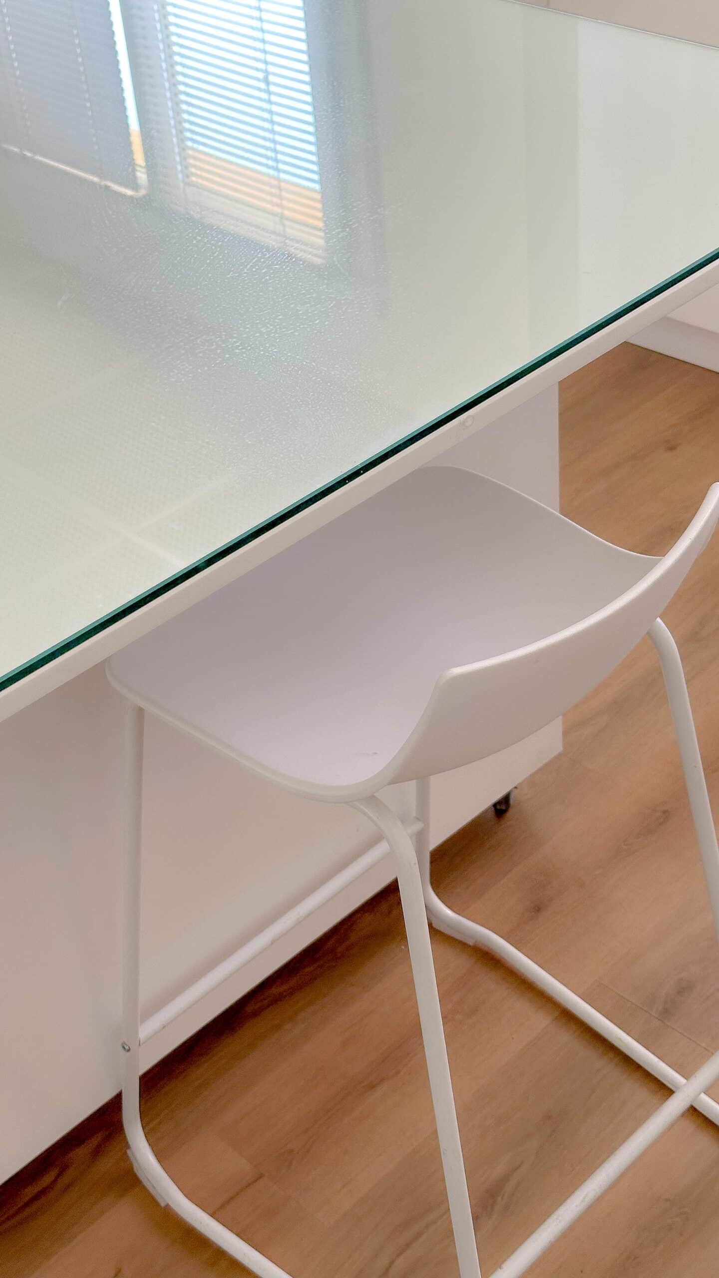 Tabouret de bar blanc moderne sous un bureau en verre dépoli et sol en parquet bois.